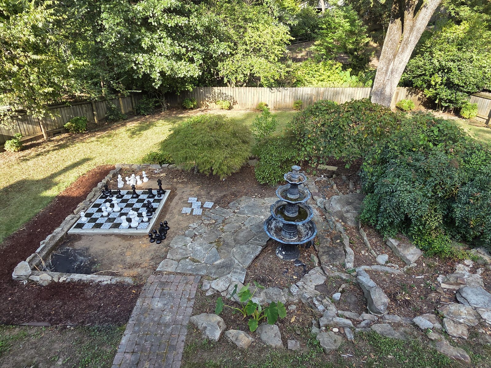 Backyard with an outdoor chessboard, flagstone path, mulch beds and a tiered fountain